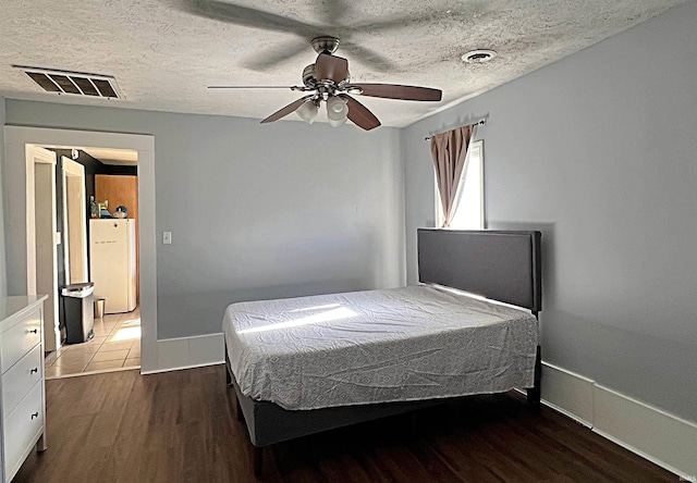 bedroom with a textured ceiling, dark hardwood / wood-style flooring, white refrigerator, and ceiling fan