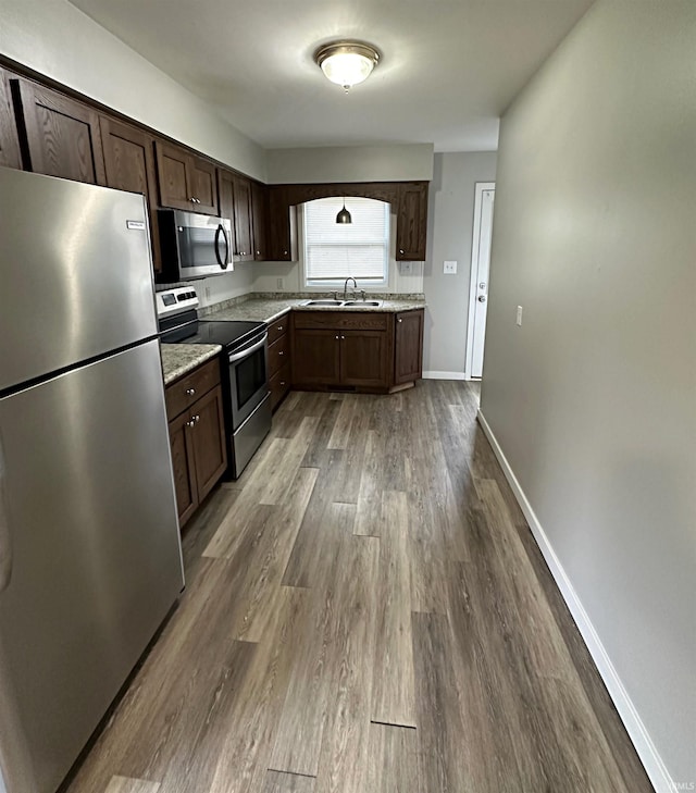 kitchen with dark brown cabinetry, sink, light stone counters, hardwood / wood-style floors, and appliances with stainless steel finishes