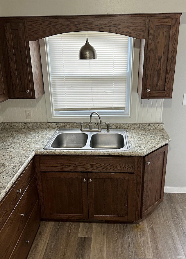 kitchen featuring dark brown cabinets, light stone counters, dark wood-type flooring, and sink