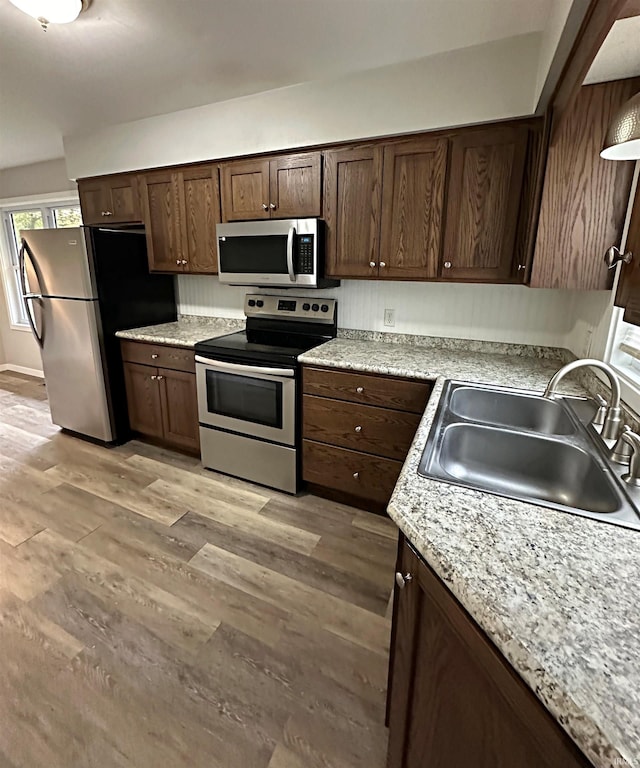 kitchen with sink, light wood-type flooring, appliances with stainless steel finishes, light stone counters, and dark brown cabinetry