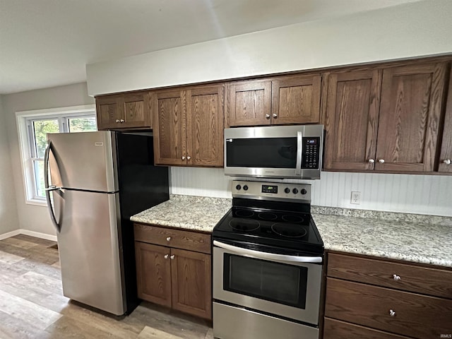 kitchen featuring dark brown cabinets, light stone countertops, appliances with stainless steel finishes, and light hardwood / wood-style flooring