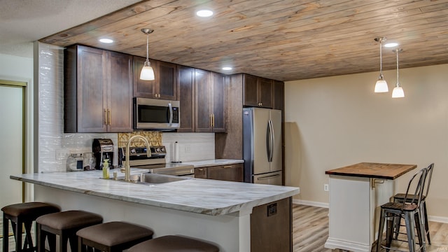 kitchen with sink, stainless steel appliances, a kitchen breakfast bar, light stone counters, and pendant lighting