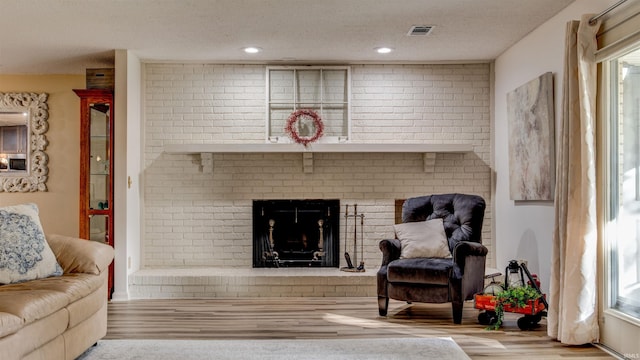 living room featuring a textured ceiling, light hardwood / wood-style floors, a brick fireplace, and brick wall