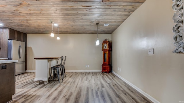 interior space with light wood-type flooring, decorative light fixtures, a kitchen bar, dark brown cabinets, and stainless steel refrigerator