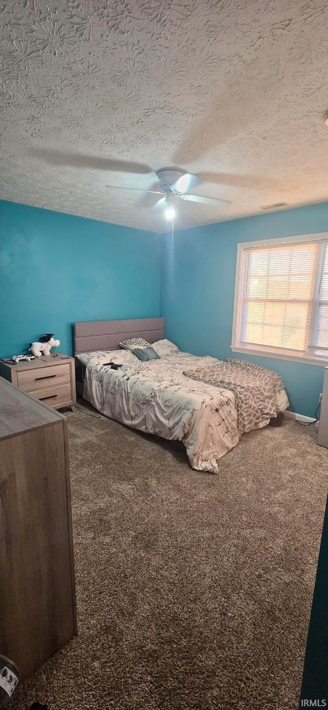 carpeted bedroom featuring ceiling fan and a textured ceiling