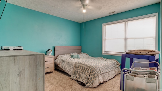 bedroom featuring a textured ceiling, light colored carpet, and ceiling fan