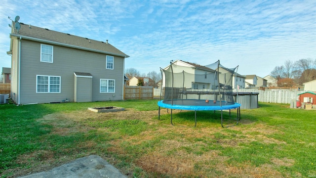 rear view of house with a lawn, a fire pit, a trampoline, central air condition unit, and a fenced in pool