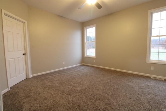 unfurnished room with dark carpet, ceiling fan, and a healthy amount of sunlight