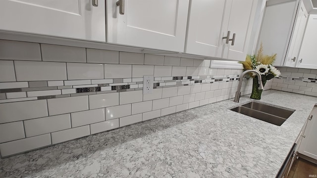 interior details featuring backsplash, white cabinetry, sink, and light stone counters