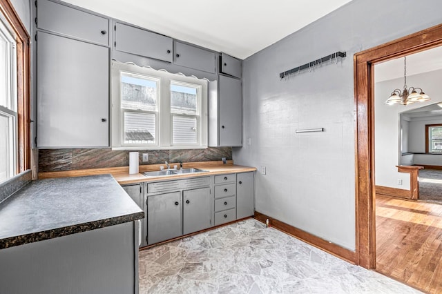 kitchen with gray cabinetry, an inviting chandelier, sink, light wood-type flooring, and tasteful backsplash