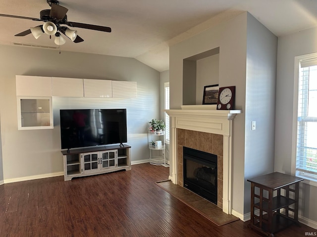 living room with dark hardwood / wood-style floors, a healthy amount of sunlight, vaulted ceiling, and a tiled fireplace