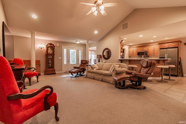 carpeted living room with decorative columns, ceiling fan, and high vaulted ceiling