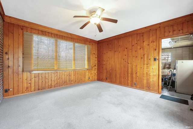 carpeted spare room featuring a healthy amount of sunlight, ornamental molding, and wooden walls