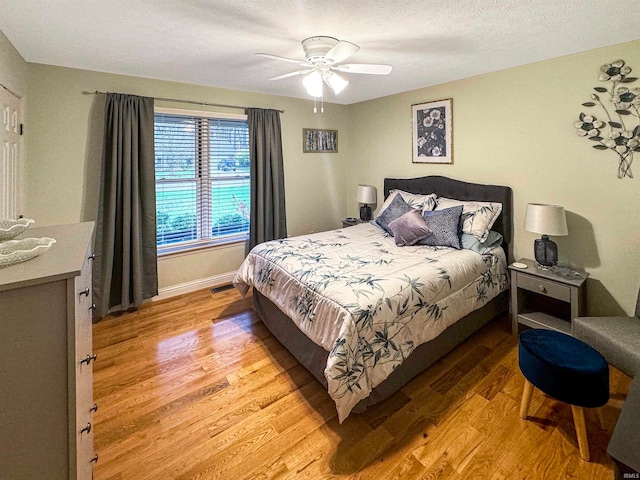 bedroom with ceiling fan, light hardwood / wood-style floors, and a textured ceiling