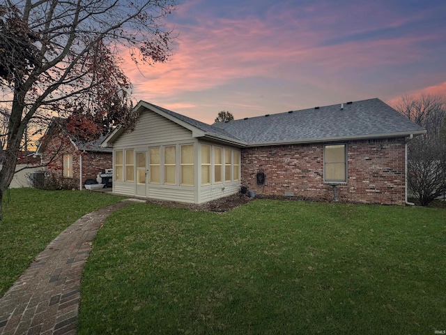 back house at dusk with a lawn and a sunroom