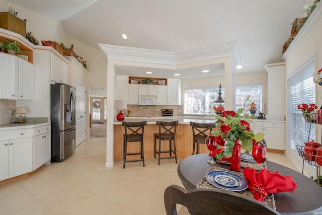 kitchen with a kitchen breakfast bar, white cabinetry, stainless steel refrigerator, and tasteful backsplash