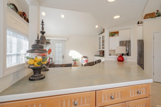 kitchen with lofted ceiling, white cabinets, stainless steel fridge, light tile patterned floors, and kitchen peninsula