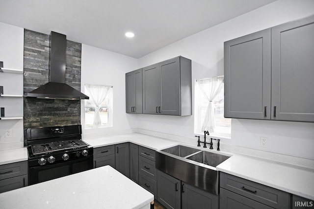 kitchen with wall chimney range hood, sink, decorative backsplash, gray cabinets, and gas stove