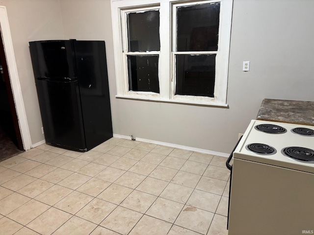 kitchen featuring black refrigerator, light tile patterned floors, and white range with electric stovetop