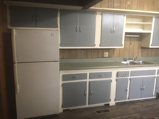 kitchen with sink, wooden walls, gray cabinets, white fridge, and dark hardwood / wood-style flooring