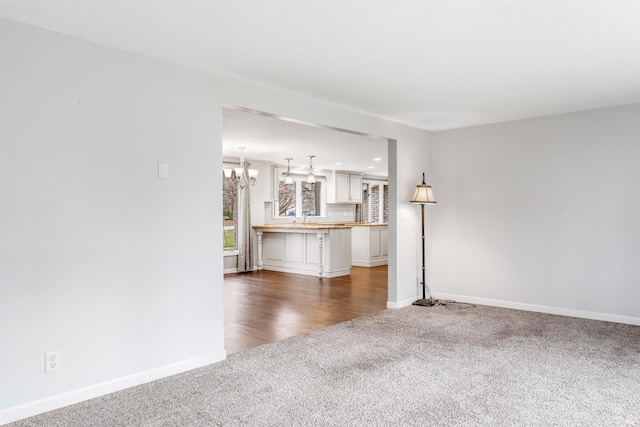 unfurnished living room with sink, dark carpet, and an inviting chandelier