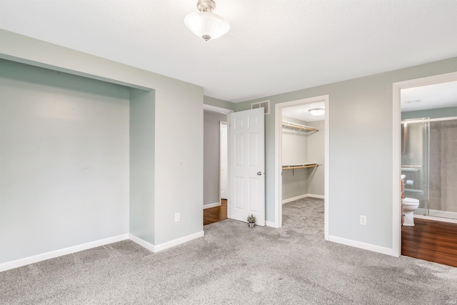 unfurnished bedroom featuring a walk in closet, ensuite bathroom, a closet, and carpet floors