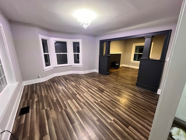 unfurnished living room with a wood stove, dark hardwood / wood-style floors, and an inviting chandelier