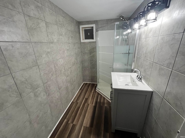 bathroom with hardwood / wood-style floors, vanity, a shower with shower door, and tile walls