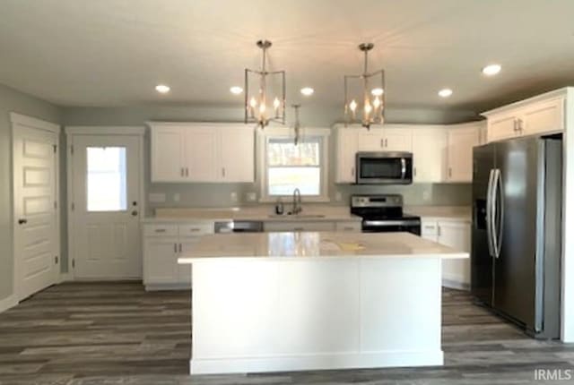 kitchen featuring appliances with stainless steel finishes, sink, white cabinets, hanging light fixtures, and a center island