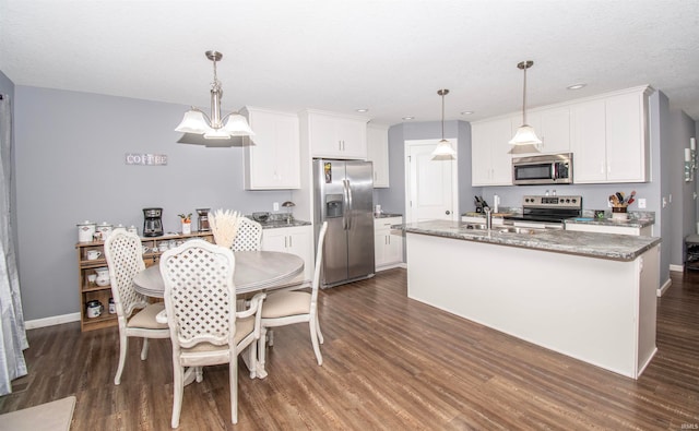 kitchen with appliances with stainless steel finishes, dark hardwood / wood-style flooring, a kitchen island with sink, decorative light fixtures, and white cabinets