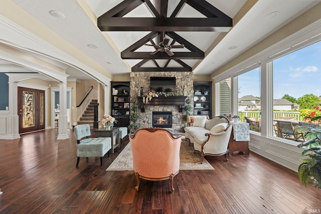 living room with built in shelves, a fireplace, ornate columns, and dark wood-type flooring