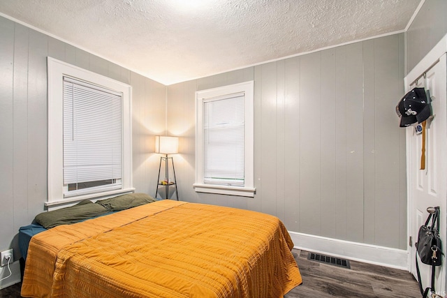 bedroom with a textured ceiling, wooden walls, and dark wood-type flooring