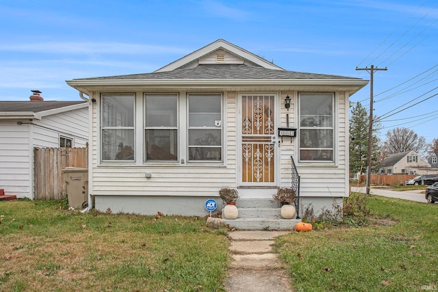 bungalow-style home featuring roof with shingles, fence, and a front yard