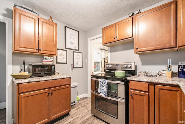 kitchen with stainless steel electric stove, light stone countertops, light hardwood / wood-style flooring, and a textured ceiling