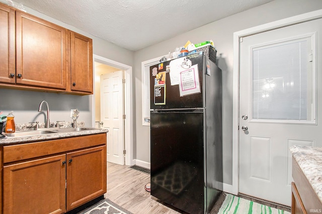 kitchen with a textured ceiling, light hardwood / wood-style floors, black fridge, and sink