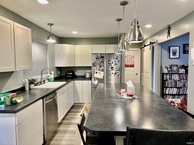 kitchen with appliances with stainless steel finishes, sink, a barn door, decorative light fixtures, and white cabinets