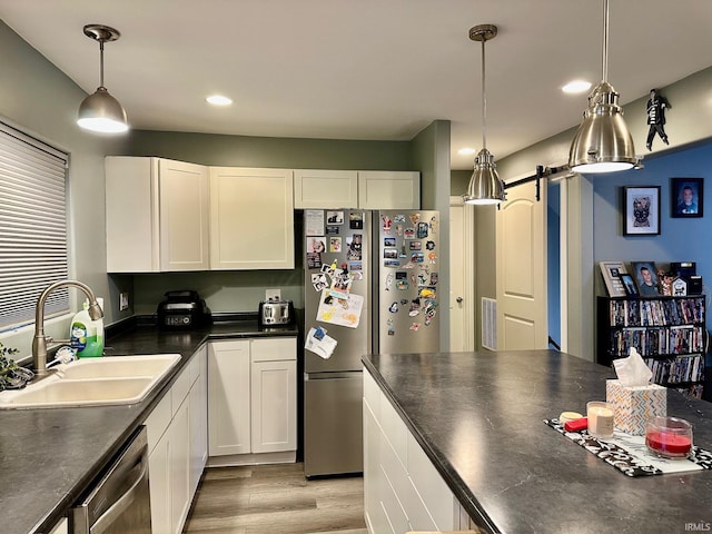 kitchen featuring white cabinetry, sink, stainless steel appliances, a barn door, and pendant lighting