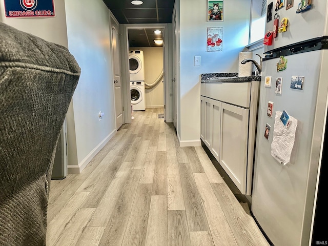 kitchen with white cabinetry, stainless steel fridge, stacked washer and dryer, dark stone counters, and light hardwood / wood-style floors