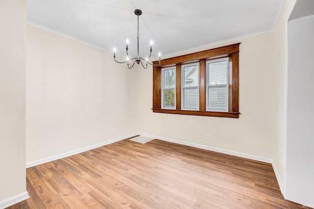 empty room featuring wood-type flooring, ornamental molding, and a chandelier