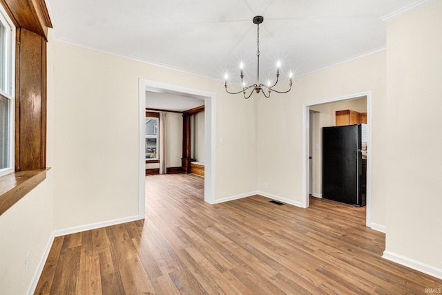 unfurnished dining area featuring a chandelier, wood-type flooring, and crown molding