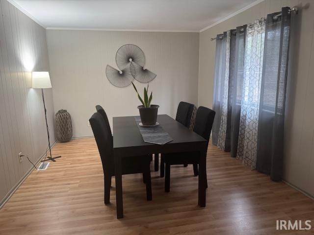 dining area with hardwood / wood-style flooring, ornamental molding, and wooden walls