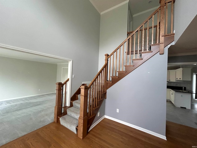 stairway featuring hardwood / wood-style flooring, ornamental molding, and a towering ceiling