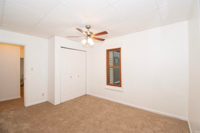 unfurnished bedroom with ceiling fan, a drop ceiling, light carpet, and a closet