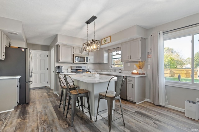 kitchen with hardwood / wood-style floors, sink, gray cabinets, decorative light fixtures, and stainless steel appliances