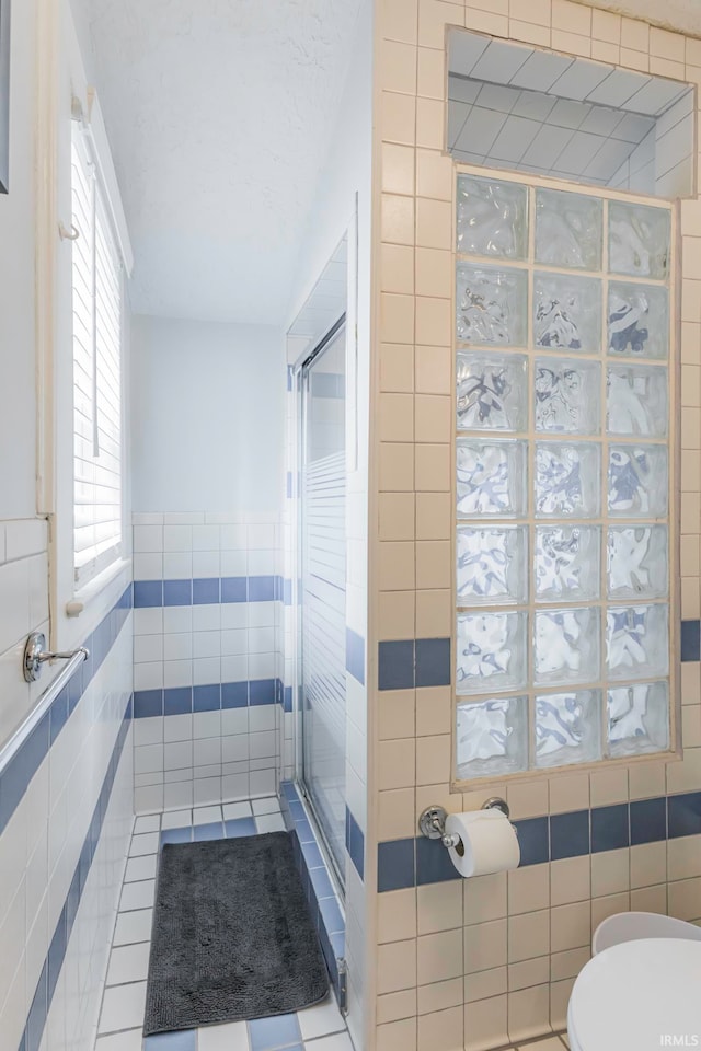 bathroom with tile patterned flooring, toilet, tile walls, and walk in shower