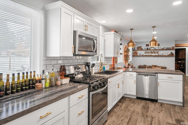 kitchen featuring stainless steel appliances, sink, light hardwood / wood-style flooring, white cabinets, and hanging light fixtures