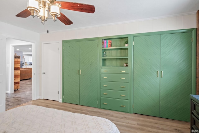 bedroom featuring ceiling fan, light wood-type flooring, ornamental molding, and two closets