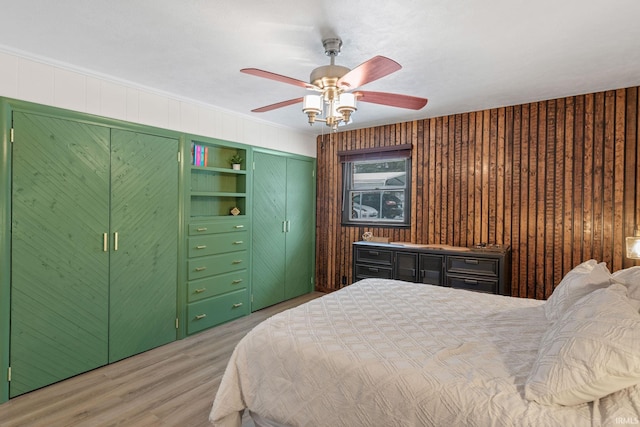 bedroom with ceiling fan, wood walls, crown molding, and light hardwood / wood-style flooring