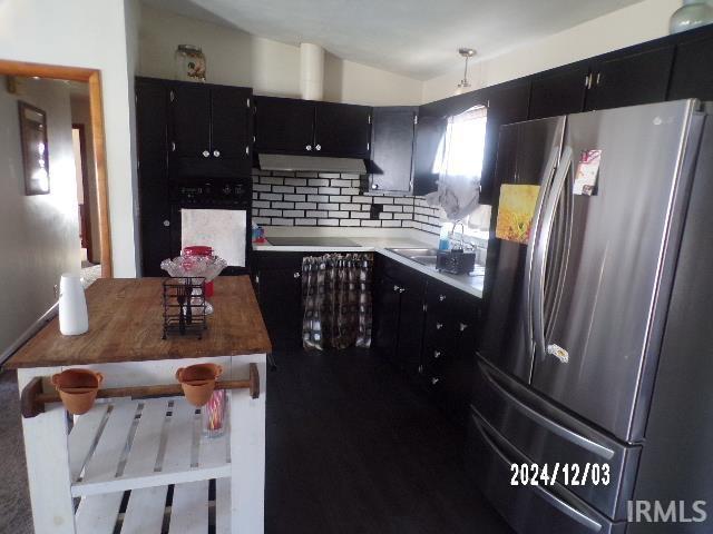 kitchen featuring decorative backsplash, stainless steel fridge, black electric stovetop, oven, and hanging light fixtures