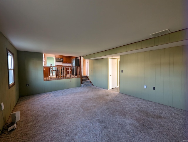 unfurnished living room featuring carpet and wooden walls